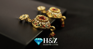 Gold earrings with red and white gemstones on a dark surface with the H&Z Diamond Centre logo